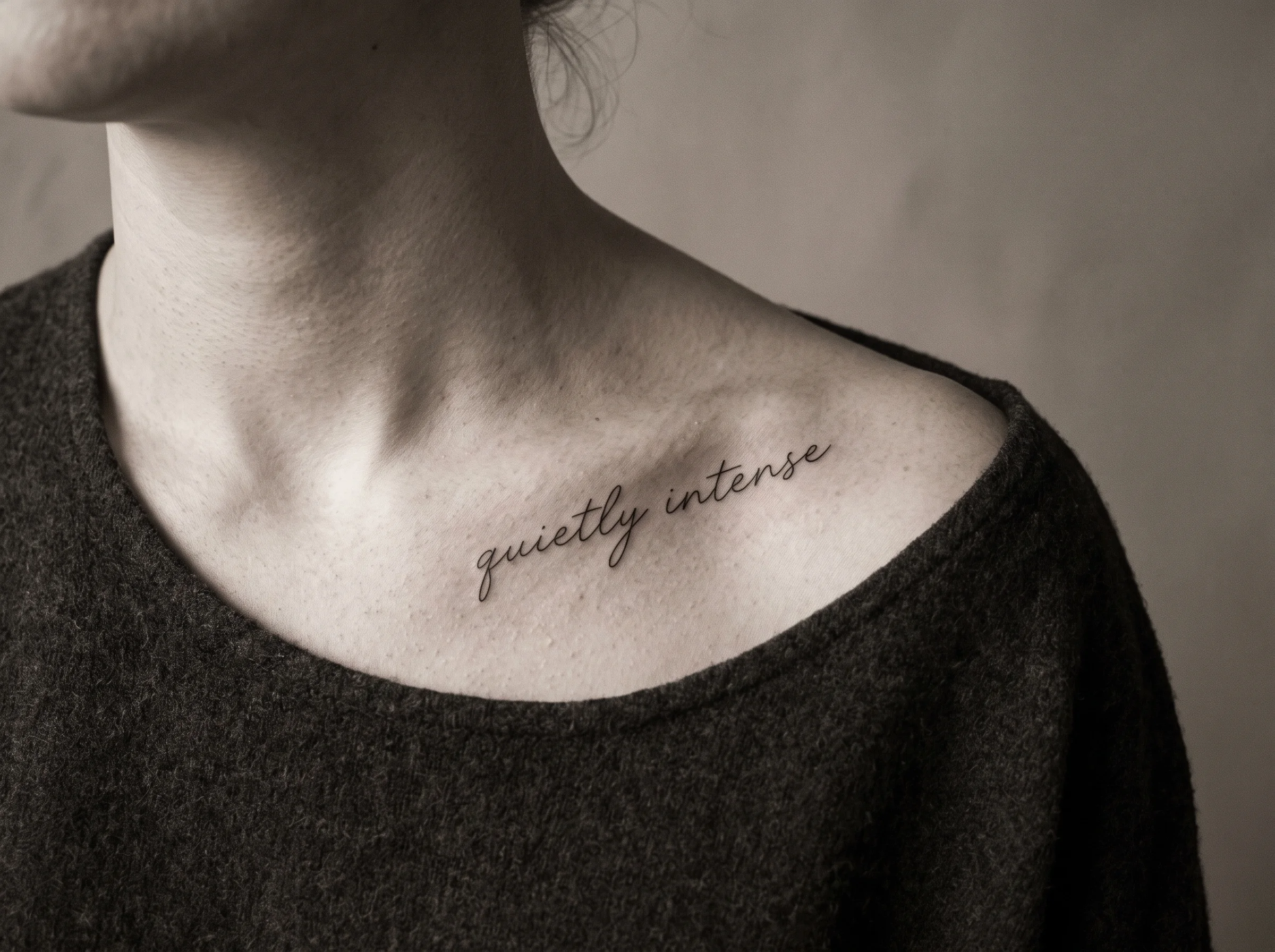 Healed fine-line script tattoo, a single line of handwriting along a collarbone in natural light